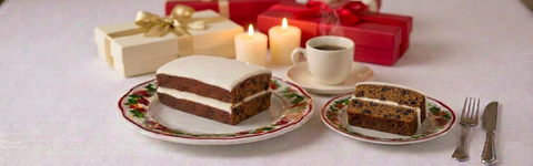 Spanish Bar Cake with white icing and a plated slice, served with coffee beside holiday candles and wrapped presents.