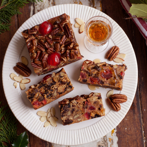 Amaretto fruitcake and slices on a white plate with sliced almonds, pecans, a glass of amaretto, and a light drizzle on one slice