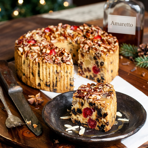 Amaretto ring fruitcake with a slice removed, served on a dark plate with almond slivers and a light drizzle, beside an amaretto bottle