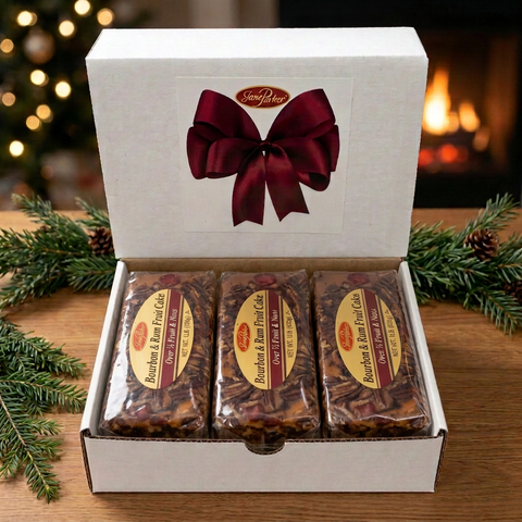 Three individually wrapped Jane Parker Bourbon & Rum Fruitcake loaves in an open white gift box with a burgundy bow design