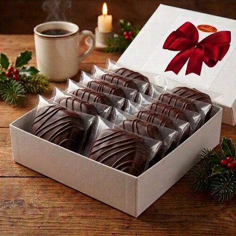 Individually wrapped dark chocolate-covered fruitcake slices arranged in an open white gift box with a red bow