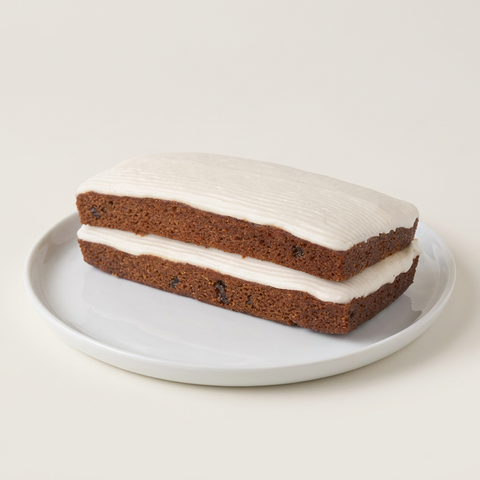 Rectangular Spanish Bar Cake with white icing on top and between two spice-cake layers, on a white plate against a neutral background.